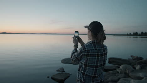Woman-Taking-Picture-of-Sunset-over-Lake-with-Smartphone